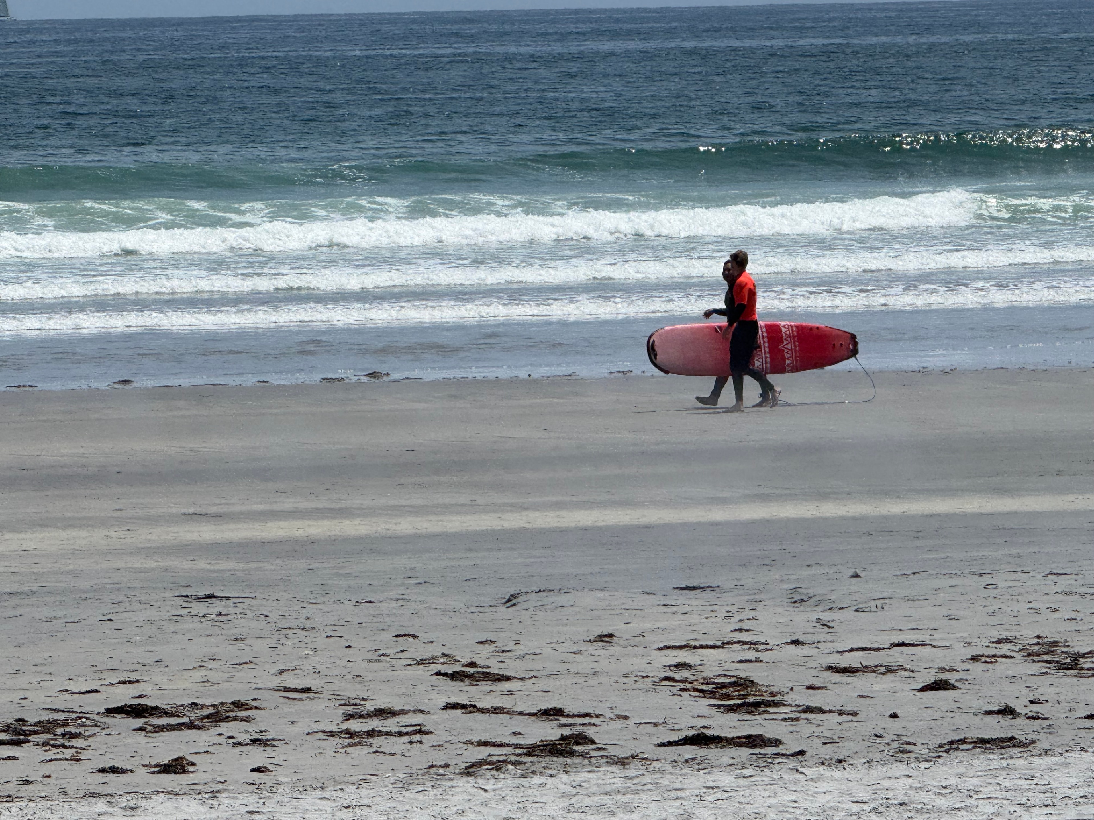 Surfers carrying a red board along the beach